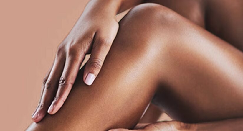 Gros plan sur une main aux ongles soignés caressant délicatement une jambe à la peau lisse et hydratée.
