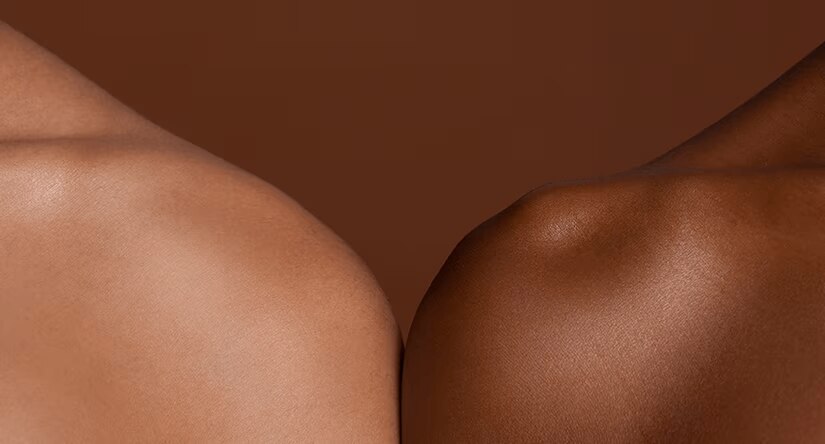 Gros plan sur les épaules de deux personnes, l'une à la peau claire et l'autre à la peau foncée, se touchant délicatement pour symboliser la diversité et la connexion.