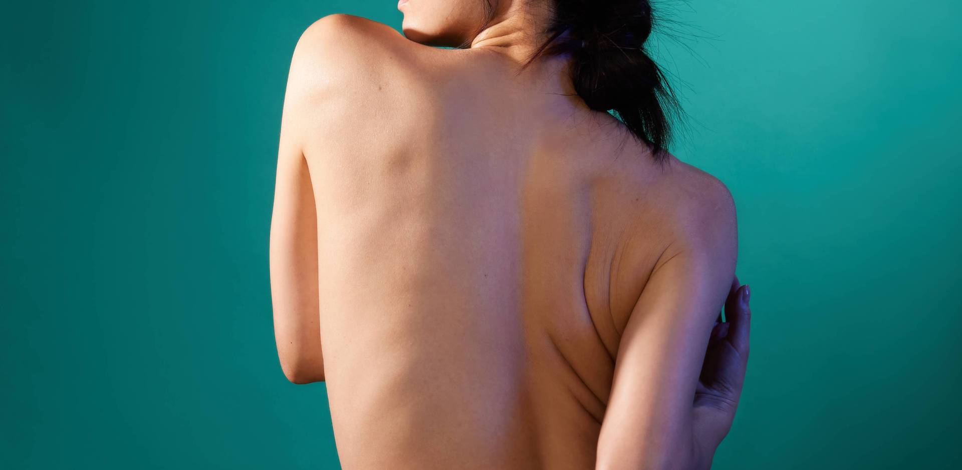 Bannière montrant la vue de dos d'une femme à la peau claire qui enlace son corps, sur un fond bleu-vert uni.