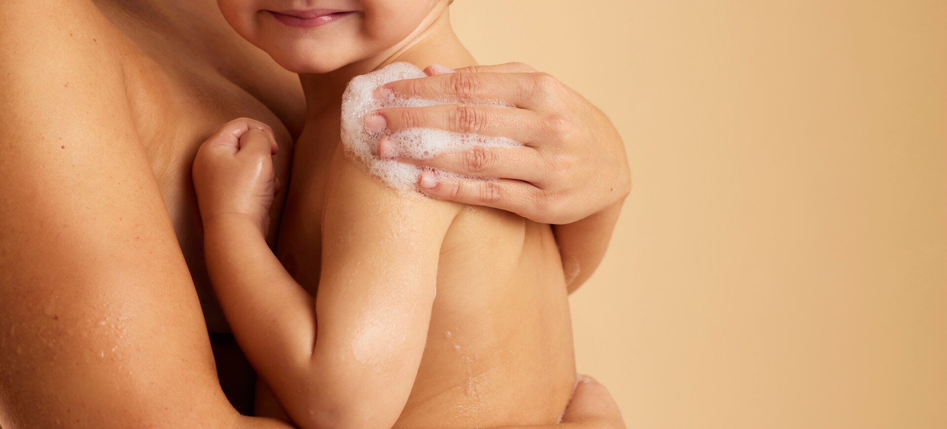 Un adulte enlace un jeune enfant et savonne délicatement son épaule avec une main pleine de mousse.