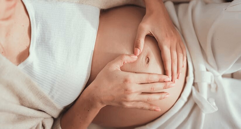 Une femme enceinte, vue de dessus, forme un cœur avec ses mains sur son ventre nu.