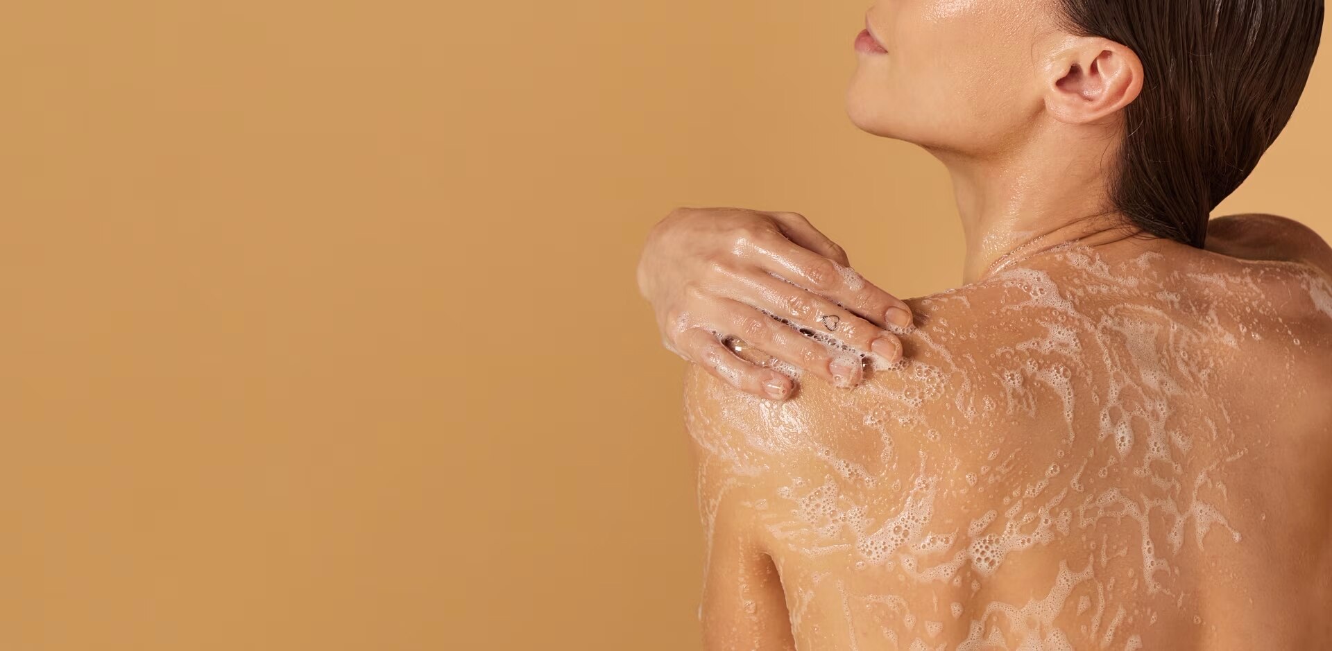 Bannière montrant une femme de dos qui se savonne l'épaule et le dos, sur un fond beige uni.