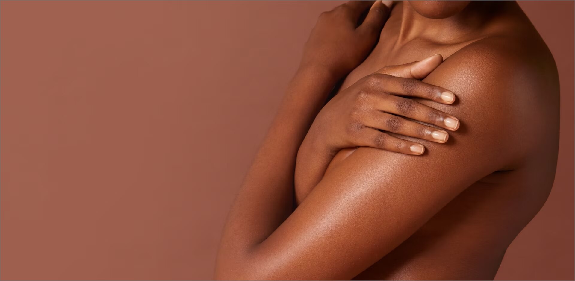 Une femme noire aux épaules nues croise les bras sur sa poitrine. Deux petites touches de crème blanche sont appliquées sur son épaule.