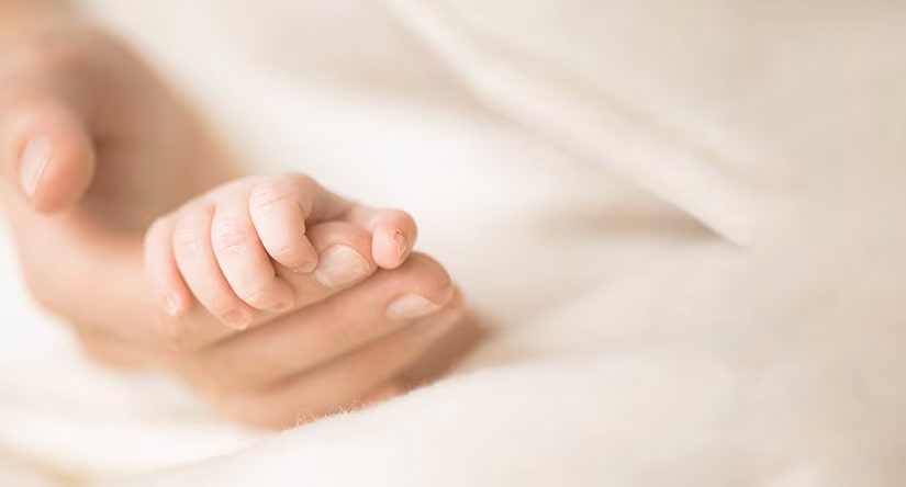 Très gros plan sur la petite main d'un nouveau-né qui s'agrippe tendrement au doigt d'un adulte.