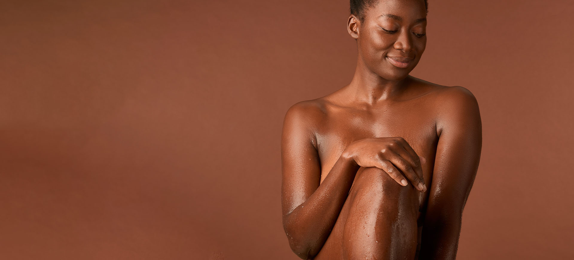gros plan d'une femme d'origine africaine nue et enlacée sur un fond de couleur peau foncée