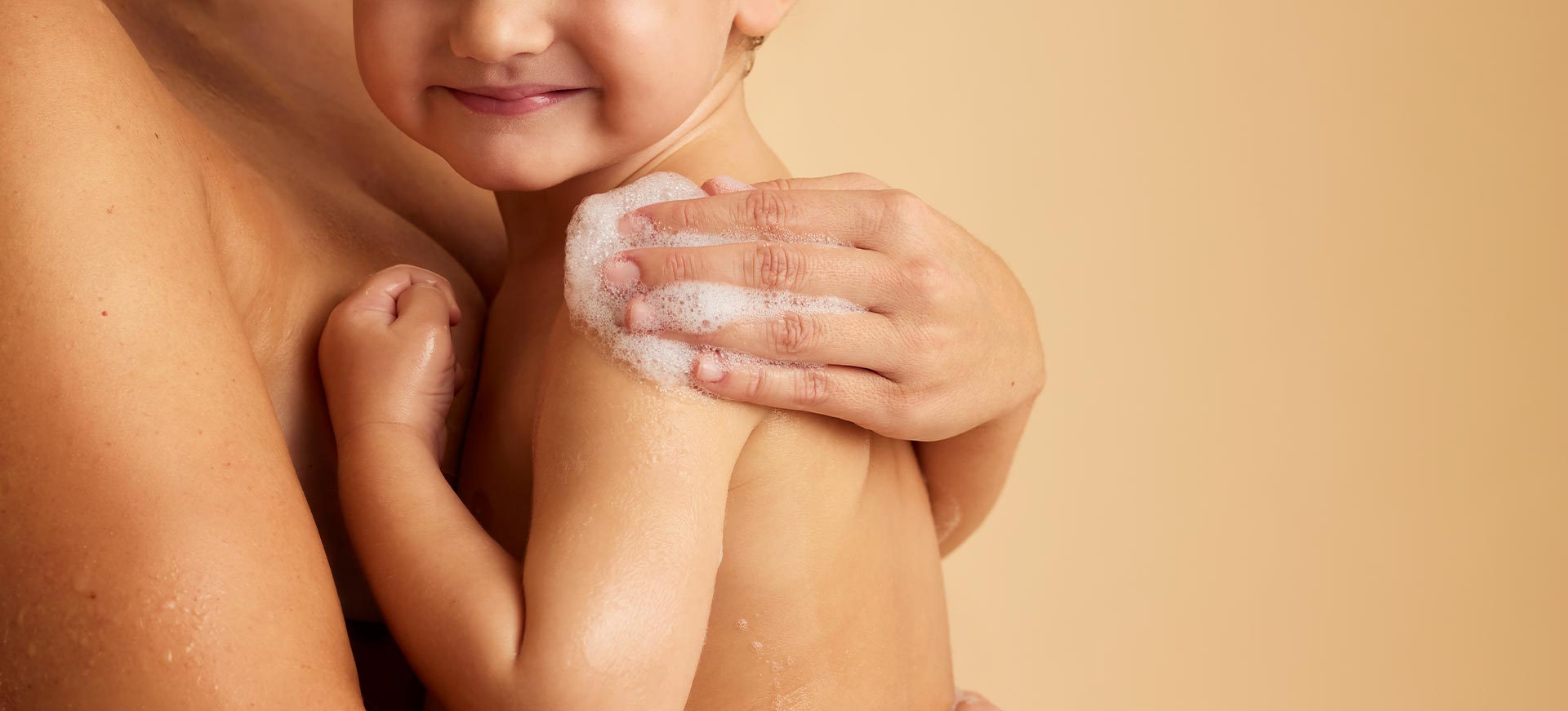 Un adulte enlace un jeune enfant et savonne délicatement son épaule avec une main pleine de mousse.