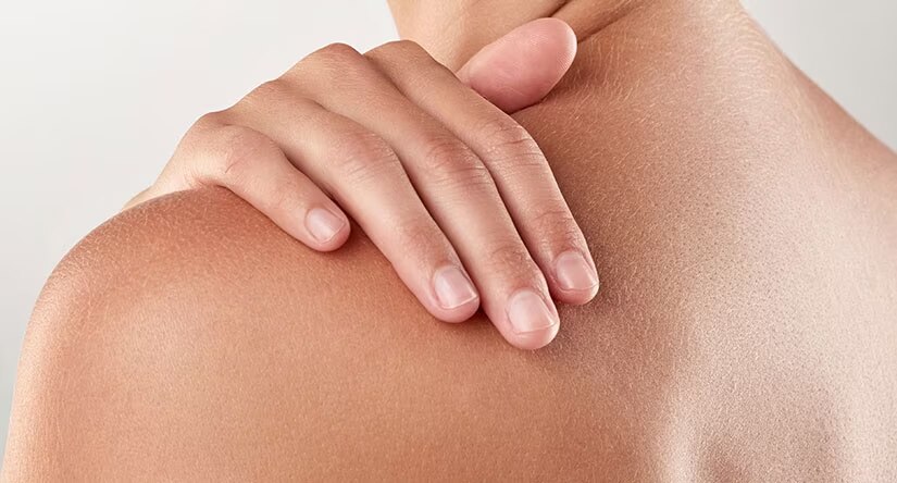Gros plan sur une main aux ongles soignés posée délicatement sur une épaule à la peau saine.