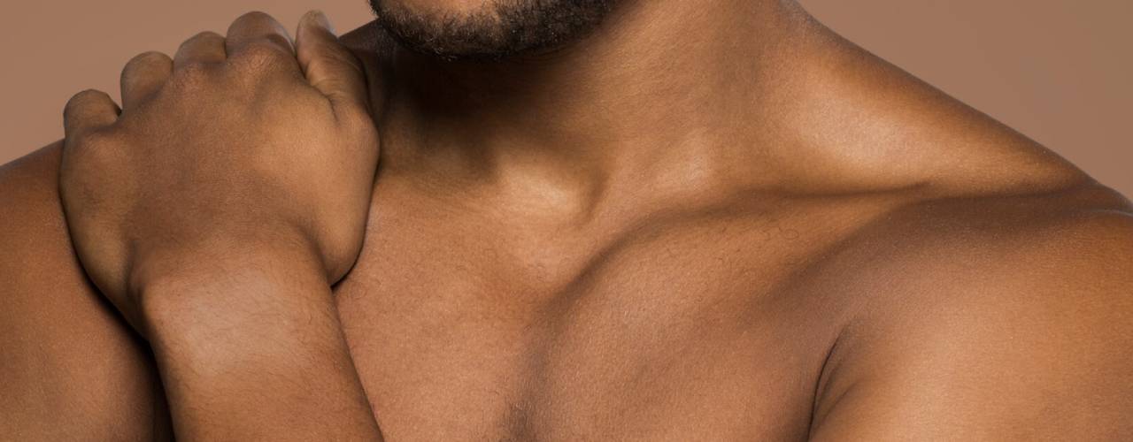 Gros plan sur le torse nu et la clavicule d'un homme noir, sa main reposant sur son épaule.