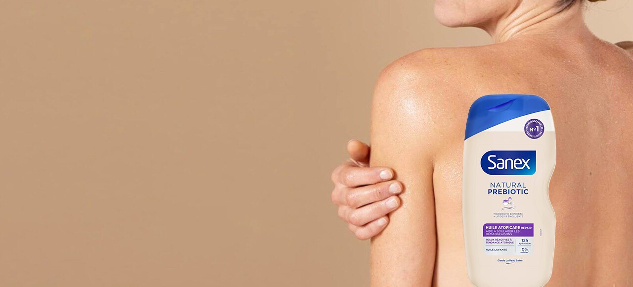 Bannière publicitaire montrant une femme de dos, sa main posée sur son épaule. Un flacon d'huile lavante Sanex Natural Prebiotic Atopicare Repair est superposé sur l'image.