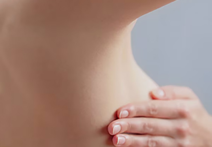 Gros plan sur le buste d'une femme à la peau claire, un bras levé montrant une aisselle lisse, l'autre main posée sur sa poitrine.