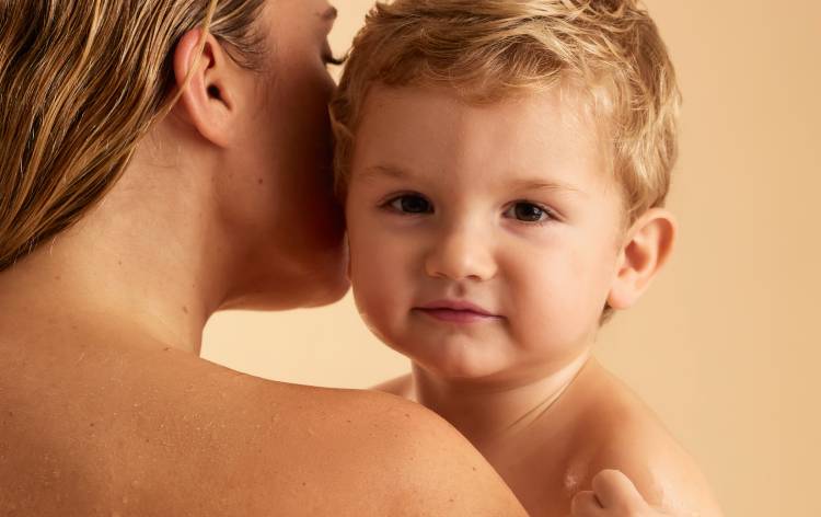 Un jeune enfant aux cheveux blonds regarde par-dessus l'épaule d'un adulte qui le tient dans ses bras.