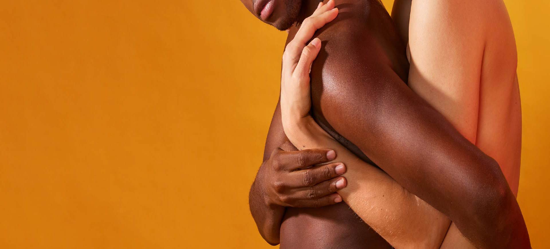 Deux personnes aux couleurs de peau différentes s'enlacent tendrement sur un fond jaune orangé vif.