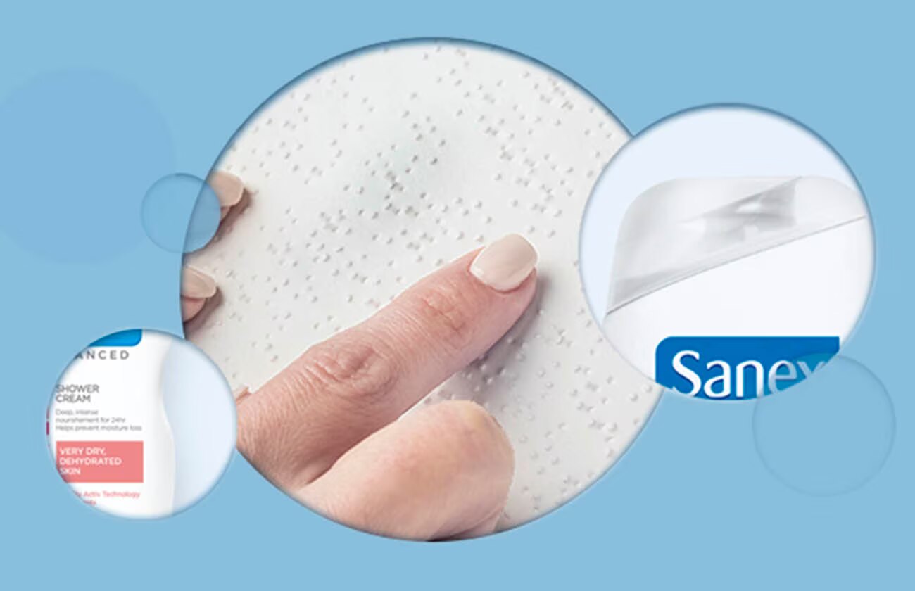 Photomontage conceptuel. Au centre, un doigt touche une surface avec des points en braille. Des extraits de produits Sanex Advanced sont visibles dans des cercles plus petits, symbolisant l'accessibilité et le soin des peaux sensibles.
