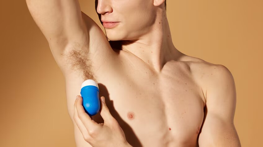 Gros plan sur un homme au torse nu qui lève le bras pour s'appliquer un déodorant roll-on bleu sur son aisselle.